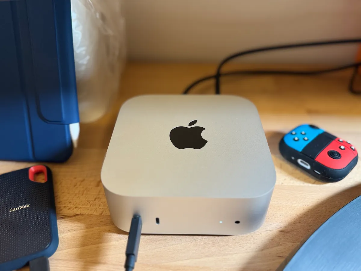 木製デスク上のMac mini M4と、SanDisk SSD、Joy-Con型カバーを付けたAir Pods Pro3、iPad Pro。前面のUSB-Cポートにケーブルが接続され、電源LEDが点灯している。