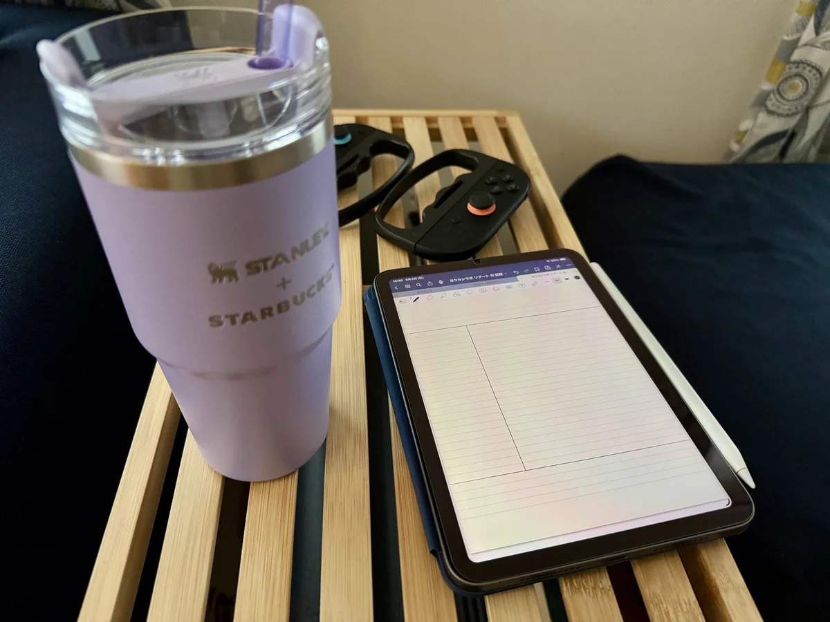 ソファ横のテーブルに、ストロー付きタンブラー・Joy-Conグリップ・手書きメモを開いたiPad miniとApple Pencilが並んでいる