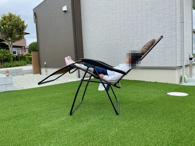 コールマン インフィニティチェアに子どもが座り、背もたれを起こした状態で庭の人工芝の上にいる